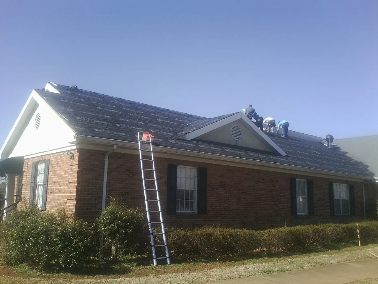 Crew tearing shingles off a brick ranch roof with a ladder set — Metal Roof Repair work by our crew in Downey
